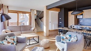 Un salon moderne avec un canapé, des fauteuils et une table basse. Un escalier mène à un autre niveau.