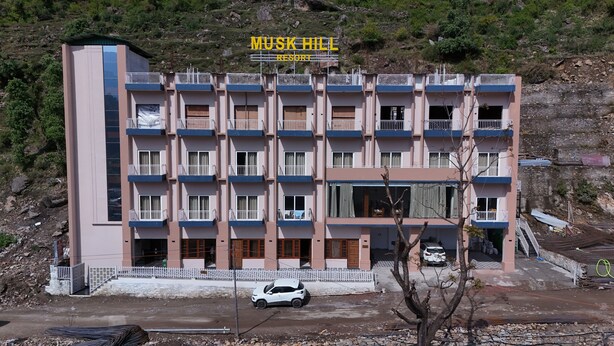 Ένα πολυώροφο κτίριο με μπαλκόνια, μια πινακίδα που γράφει «MUSK HILL RESORT» και ένα σταθμευμένο αυτοκίνητο μπροστά.