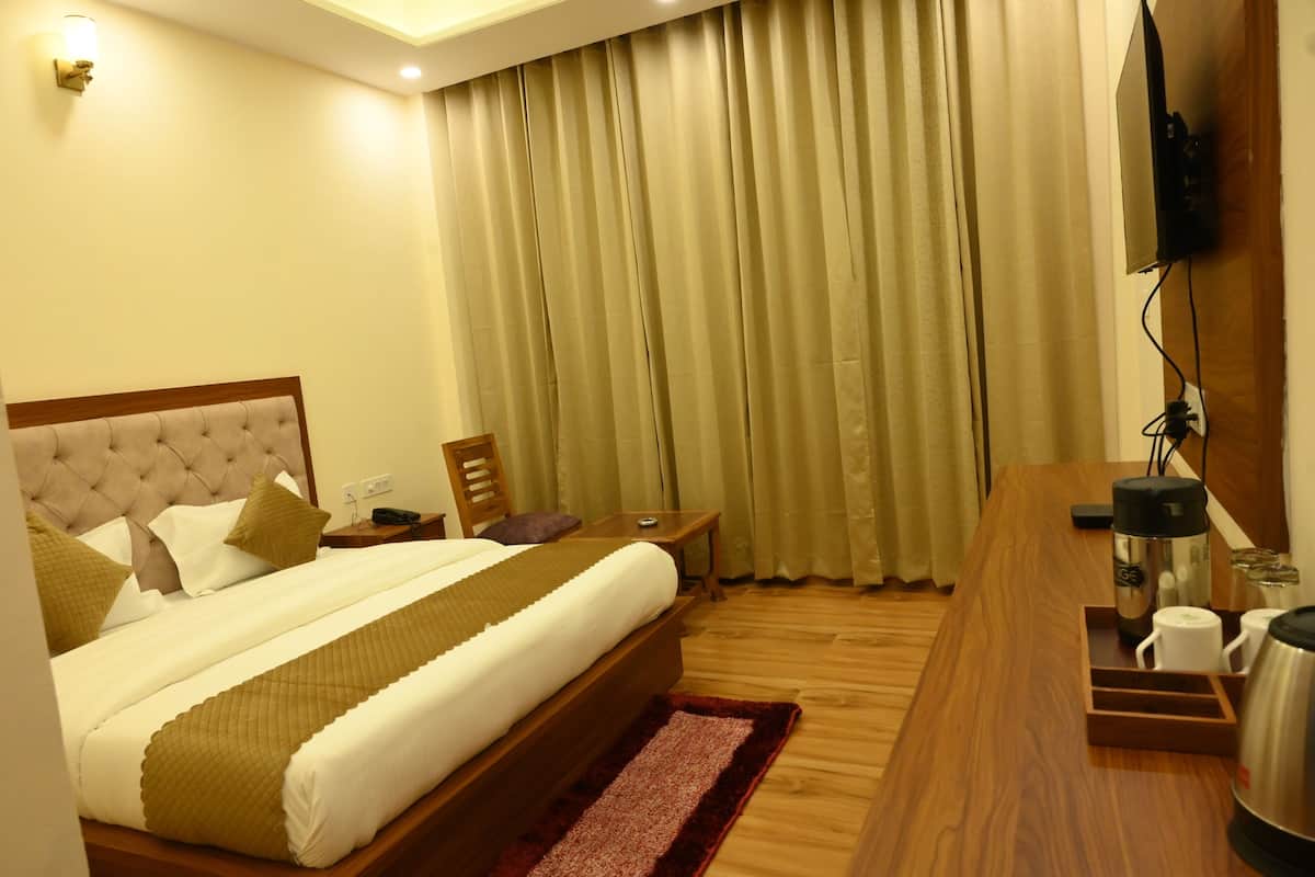 A hotel room with a large bed, wooden headboard, a bedside table, a TV mounted on the wall, and a wooden desk with a coffee maker.