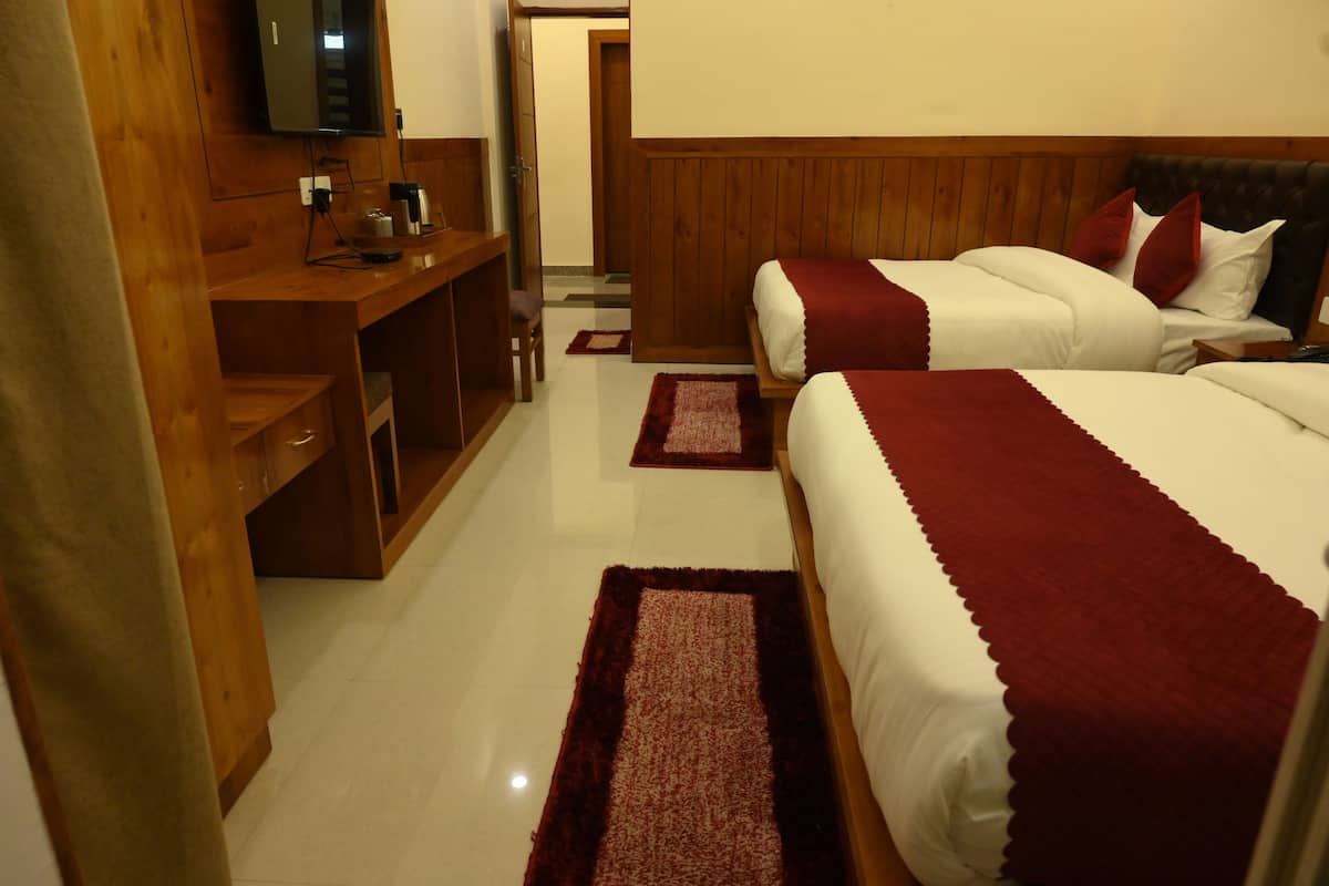 A hotel room with two beds, wooden headboards, a desk with a chair, a television, and a small table with a lamp.