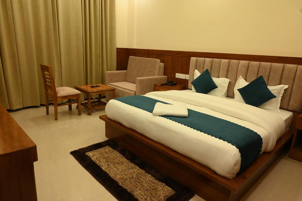 A hotel room with a large bed, two armchairs, a wooden nightstand, a desk, and a chair.