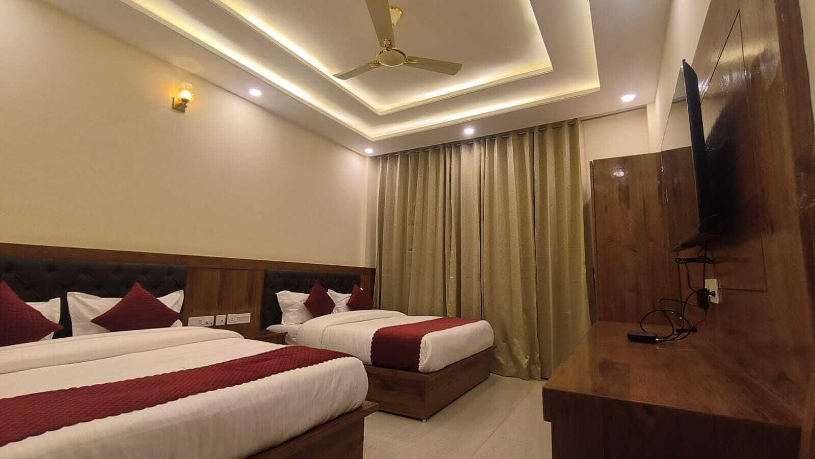 Habitación de hotel con dos camas, ventilador de techo, iluminación empotrada, televisor y un escritorio de madera.
