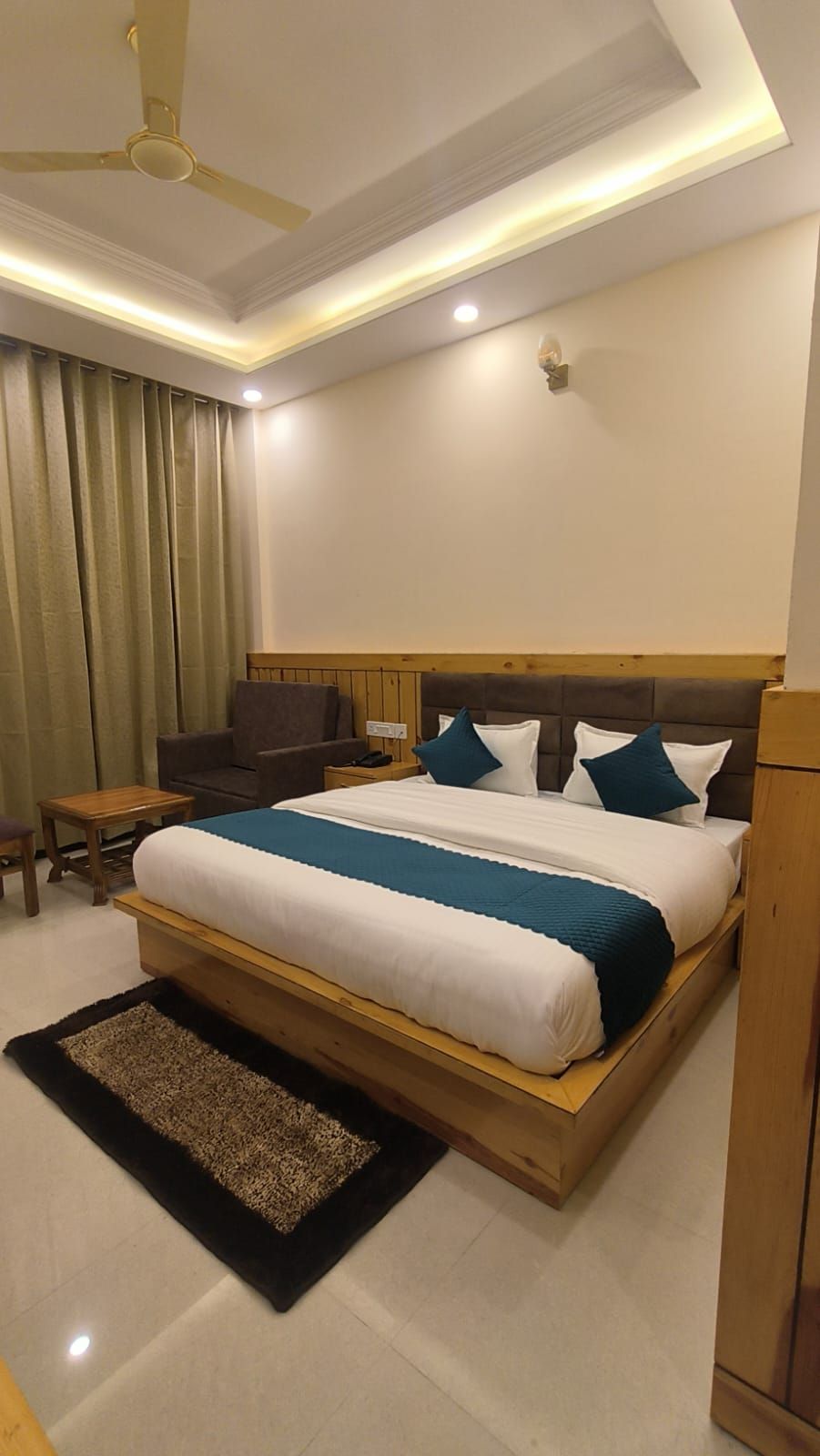 A hotel room with a large bed, a wooden headboard, a desk, a chair, and a ceiling fan.