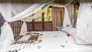 A room with a bed covered in a zebra-patterned blanket, white curtains, and a small bedside table with a lamp.