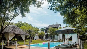 A pool area with lounge chairs, a thatched-roof structure, and a modern building in the background.