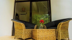 A wicker sofa with dark cushions, a glass vase with red flowers, and a view of a building through a glass door.