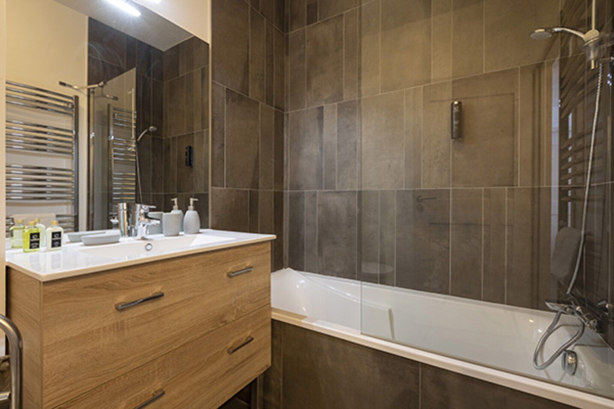 A modern bathroom with a wooden vanity, a white sink, and a bathtub.