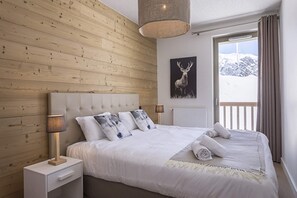 Een slaapkamer met een houten wand, een bed met witte lakens, een afbeelding van een hert aan de muur en een raam met gordijnen.