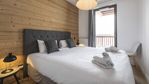 Una habitación de hotel moderna con una cama grande, un panel de pared de madera, vistas al balcón y una silla blanca.