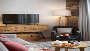 Una sala de estar moderna con un televisor de pantalla plana, muebles de madera, un sofá de cuero negro, una pared decorativa de piedra y una mesa con aperitivos.