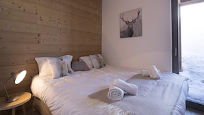Un dormitorio con pared de madera, una cama con ropa de cama blanca, un cuadro de un ciervo y una mesita de noche con una lámpara.