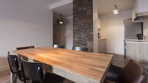 Un comedor moderno con una mesa de madera y sillas negras, una pared de acento de piedra y una cocina al fondo.