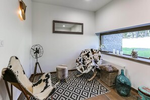 A cozy seating area with a patterned rug, a rocking chair, a fan, and a window with a view of greenery. - Apartment in La Rosière with Stunning Alpine Views (la rosiere montvalezan)