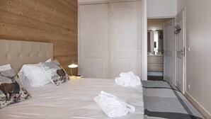 A hotel room with a wooden ceiling, a bed with white linens, a bedside lamp, and a bathroom visible through an open door.