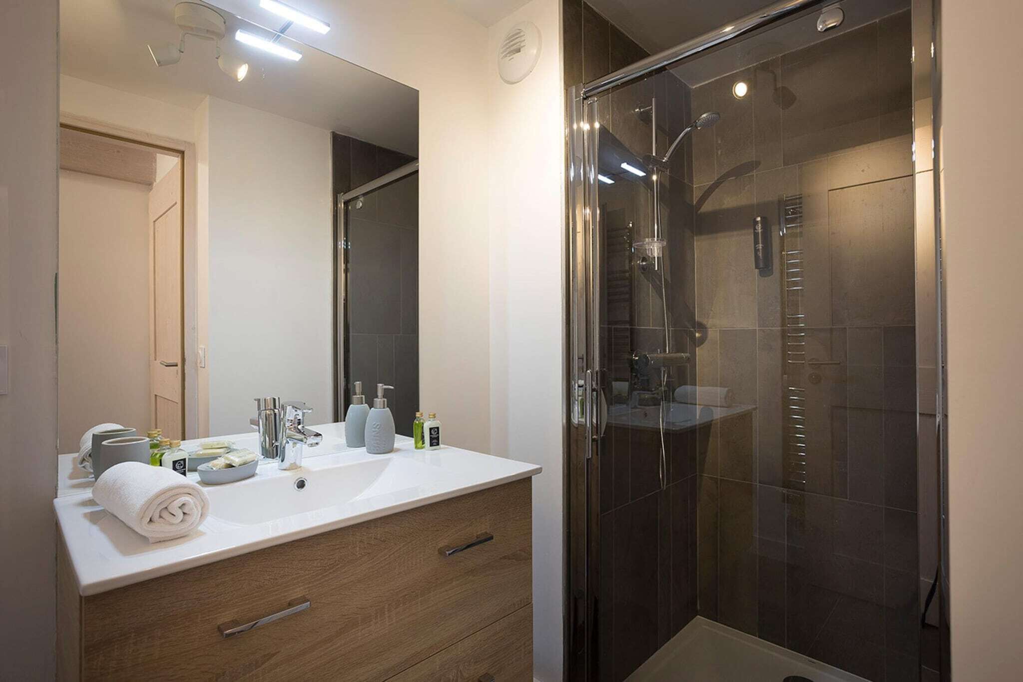 Ein modernes Badezimmer mit einer Duschkabine, einem weißen Waschbecken mit Toilettenartikeln und einem hölzernen Waschtisch.