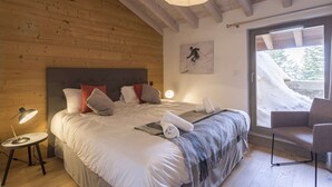 A bedroom with a large bed, a bedside lamp, a chair, and a view of a snowy landscape through a glass door. - Apartment in La Rosière with Alpine Views (la rosiere montvalezan)