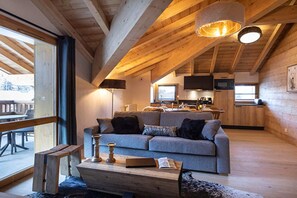 A cozy living room with a sofa, a coffee table, and a wooden bench. A kitchen with a microwave and a dining area is visible in the background. - Apartment in France near Scenic Cafes & Markets (Les Deux Alpes)