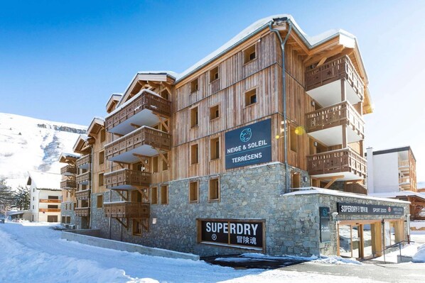A multi-story wooden building with balconies, a stone base, and signs for 'Superdry' and 'Neige & Soleil Terresens'.