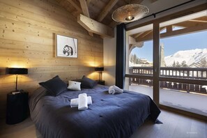 A bedroom with a large bed, wooden walls, a framed picture, and a view of a snowy mountain.