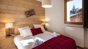 Ein gemütliches Schlafzimmer mit einem Holzkopfteil, einem großen Fenster und einer roten Tagesdecke.