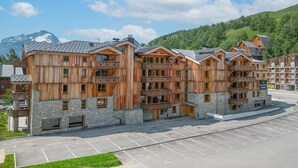 Ein mehrstöckiges Holzgebäude mit Balkonen, Steinsockeln und einem Parkplatz davor.