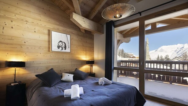 Un dormitorio con una cama grande, paredes de madera, un cuadro enmarcado y vistas a una montaña nevada.