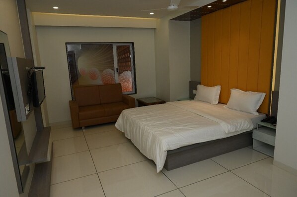A modern bedroom with a large bed, a brown armchair, a TV, and a window with a view of a building. - HOTEL PARQOTEL (Vapi)