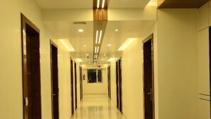 A long, well-lit hallway with shiny tiled floors and wooden doors on both sides. - HOTEL PARQOTEL (Vapi)
