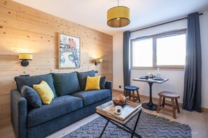 Un salon chaleureux avec un canapé bleu, des murs lambrissés, une table avec un plateau et une grande fenêtre avec des rideaux.