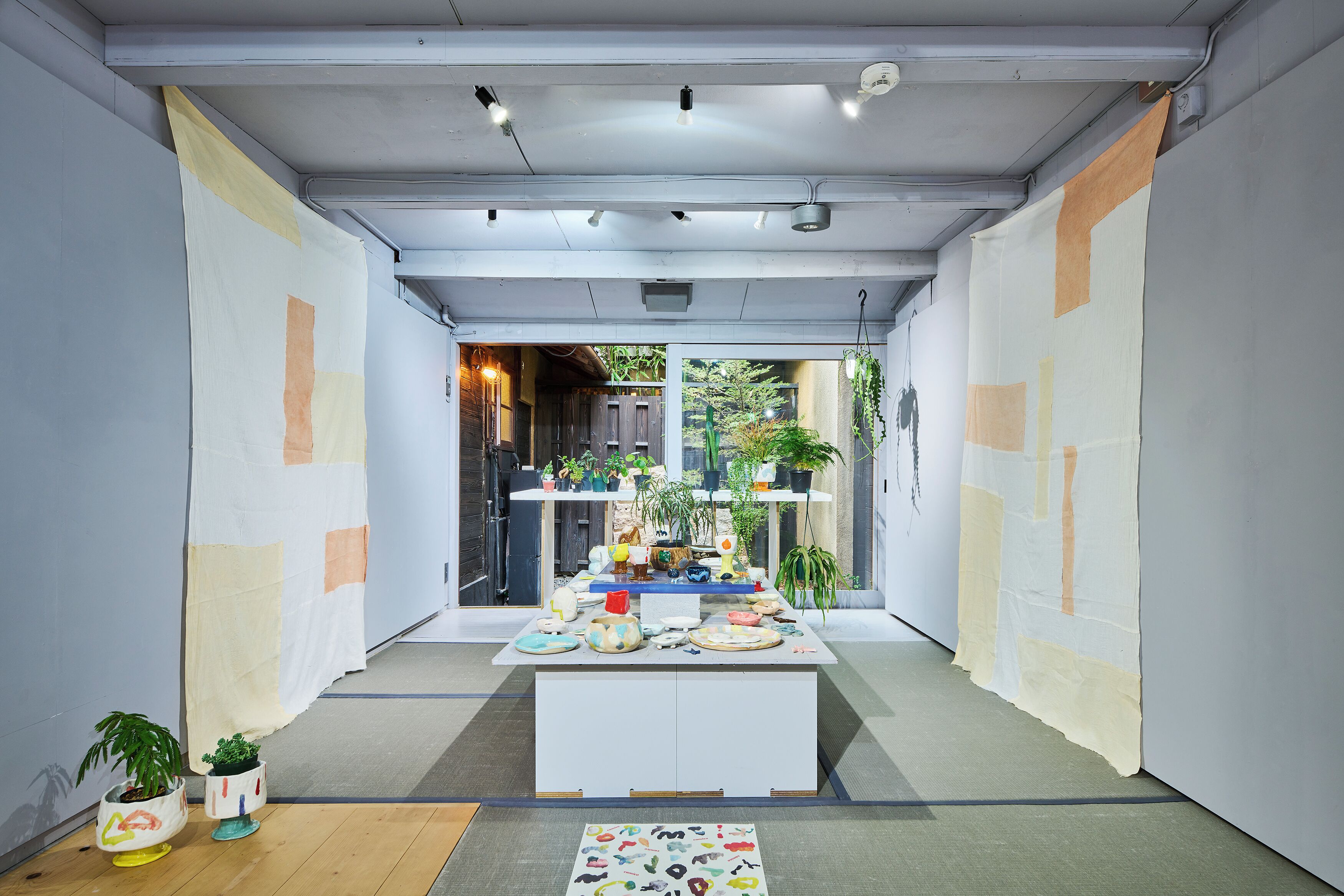 Un intérieur moderne avec une table centrale où sont exposés divers objets, le tout bordé de murs ornés d’œuvres d’art abstraites et de plantes en pot.