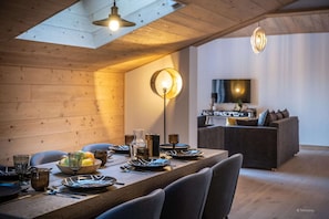 Un coin repas avec une table en bois dressée pour le repas, un canapé et un téléviseur en arrière-plan.