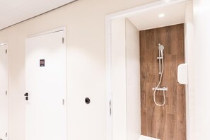 A hotel bathroom with a wooden shower wall, white doors, and a visible sign on one door.