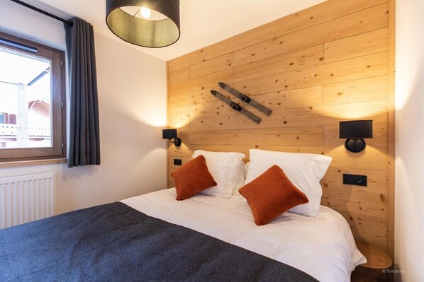 A bedroom with a wooden headboard, two bedside lamps, and a window with curtains.