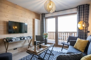 Un salon moderne doté d’un téléviseur à écran plat, de murs recouverts de panneaux en bois, d’un canapé et d’un balcon offrant une vue agréable.
