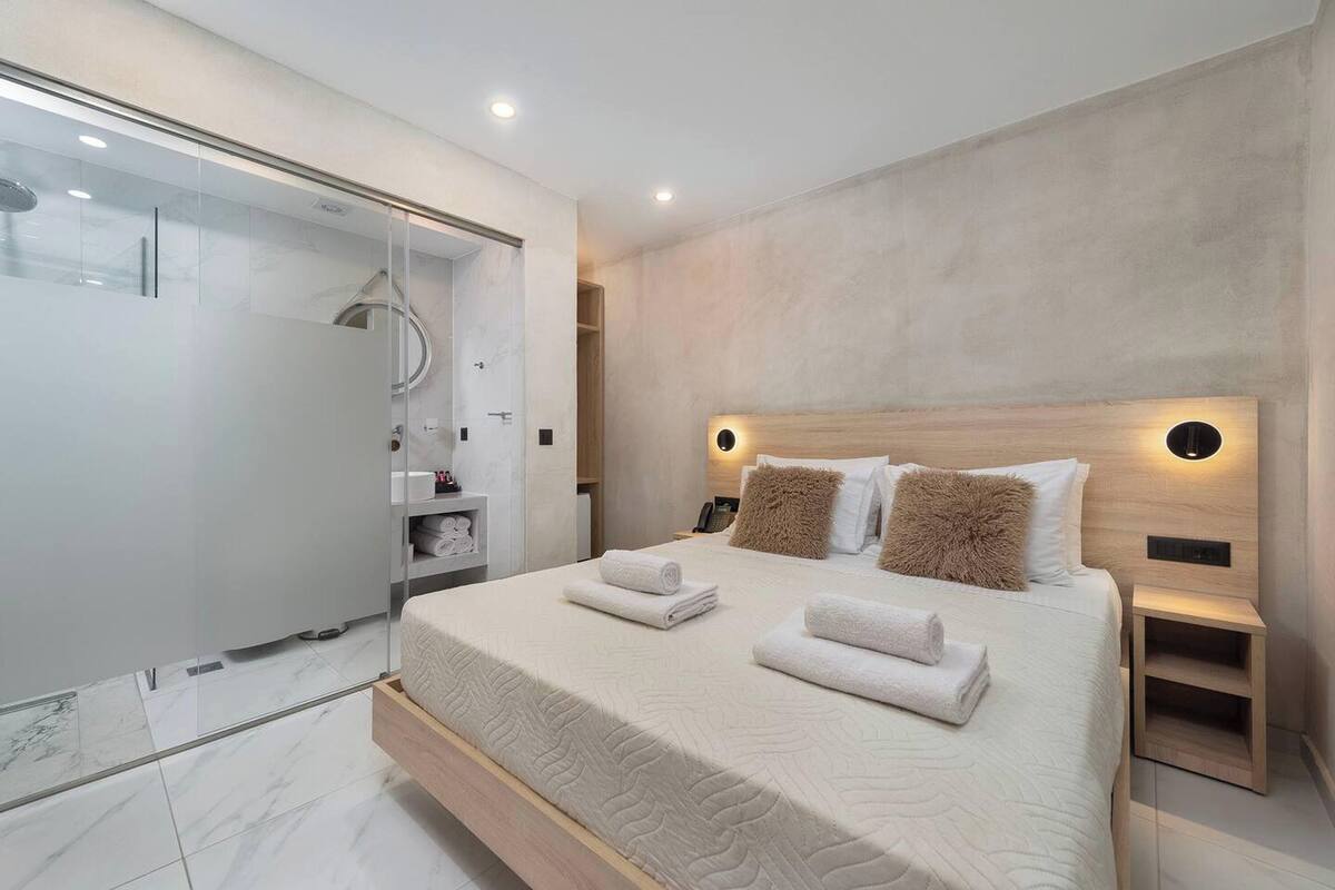 A modern bedroom with a large bed, a glass shower enclosure, and a wooden headboard.