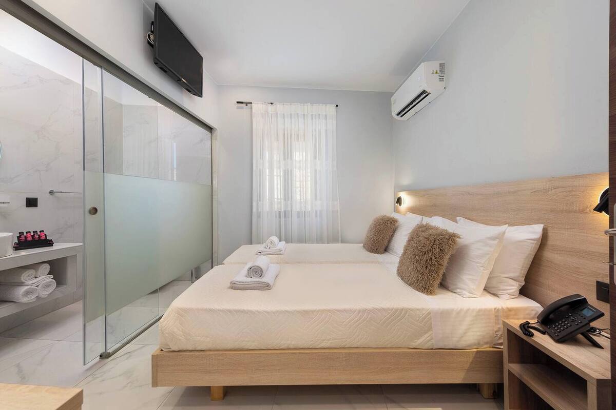 A modern hotel room with a bed, a bedside phone, a TV, and a shower area with glass doors.