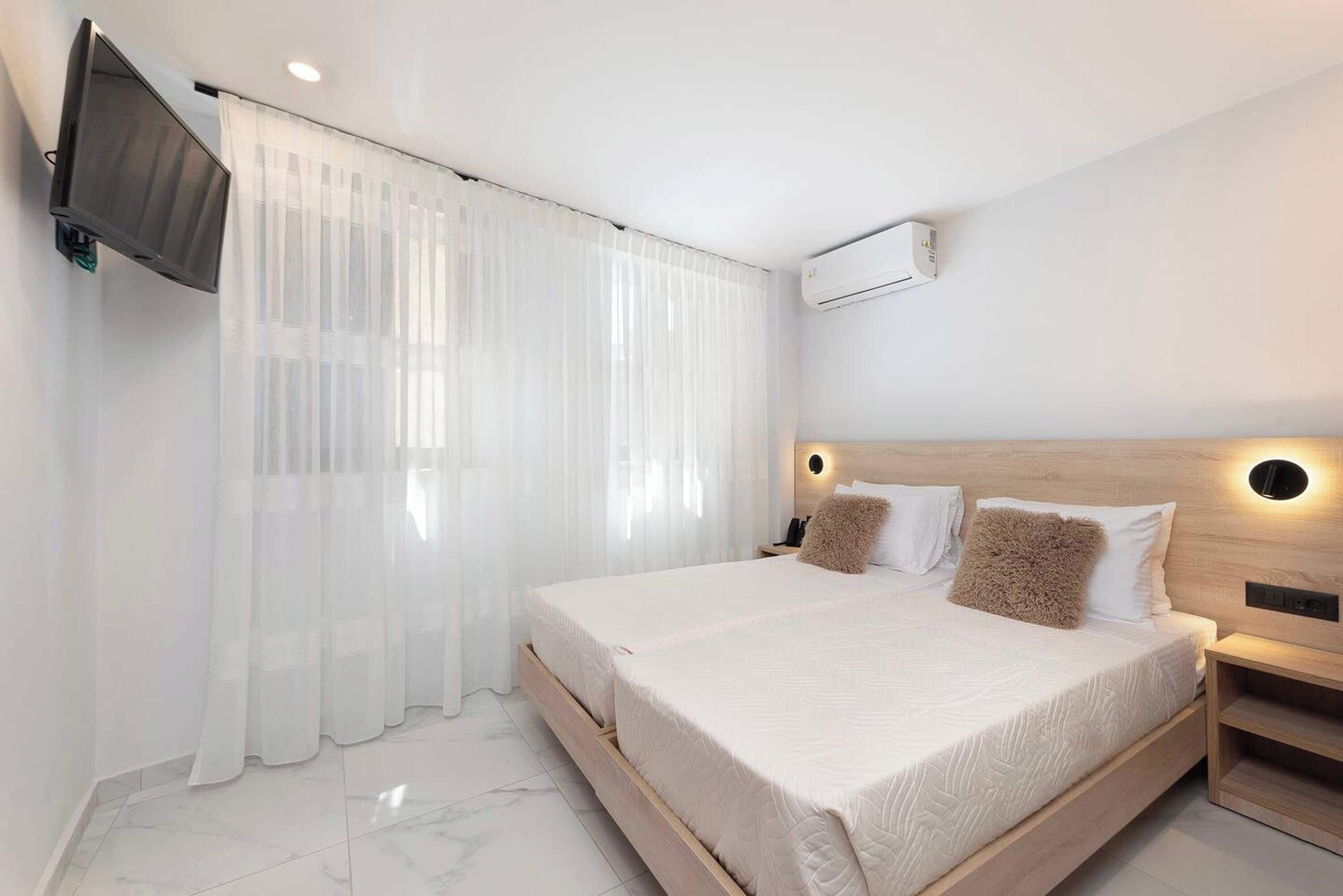 A modern bedroom with a large bed, a mounted TV, and an air conditioning unit.