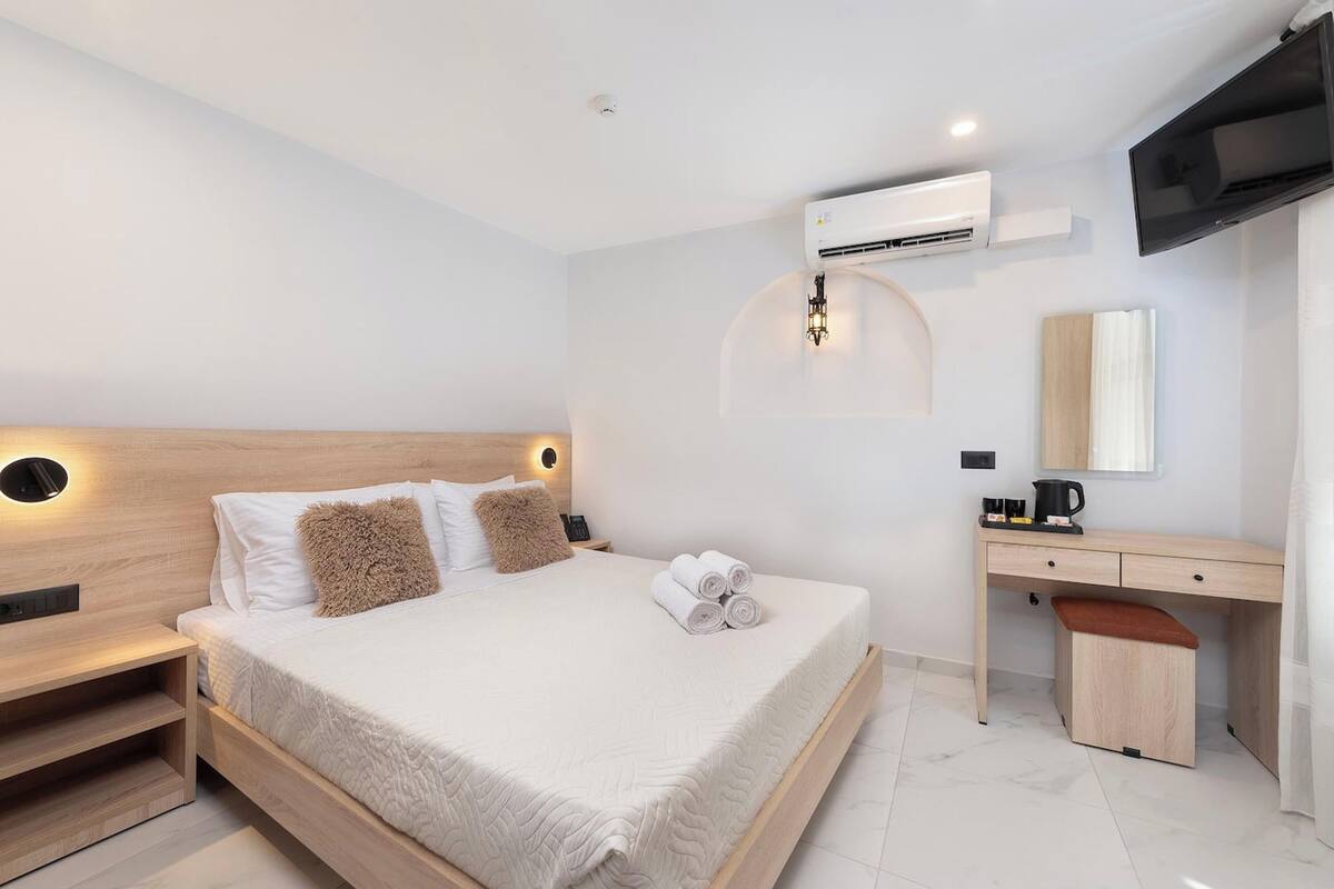 A modern hotel room with a wooden bed, a desk, a flat-screen TV, and an air conditioning unit.