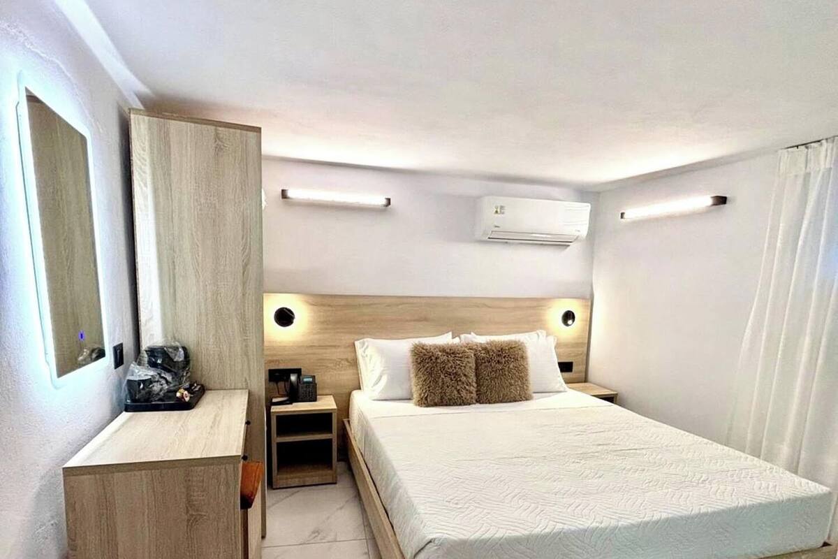 A modern hotel room with a wooden bed frame, a bedside table, a built-in wardrobe, and a large mirror.