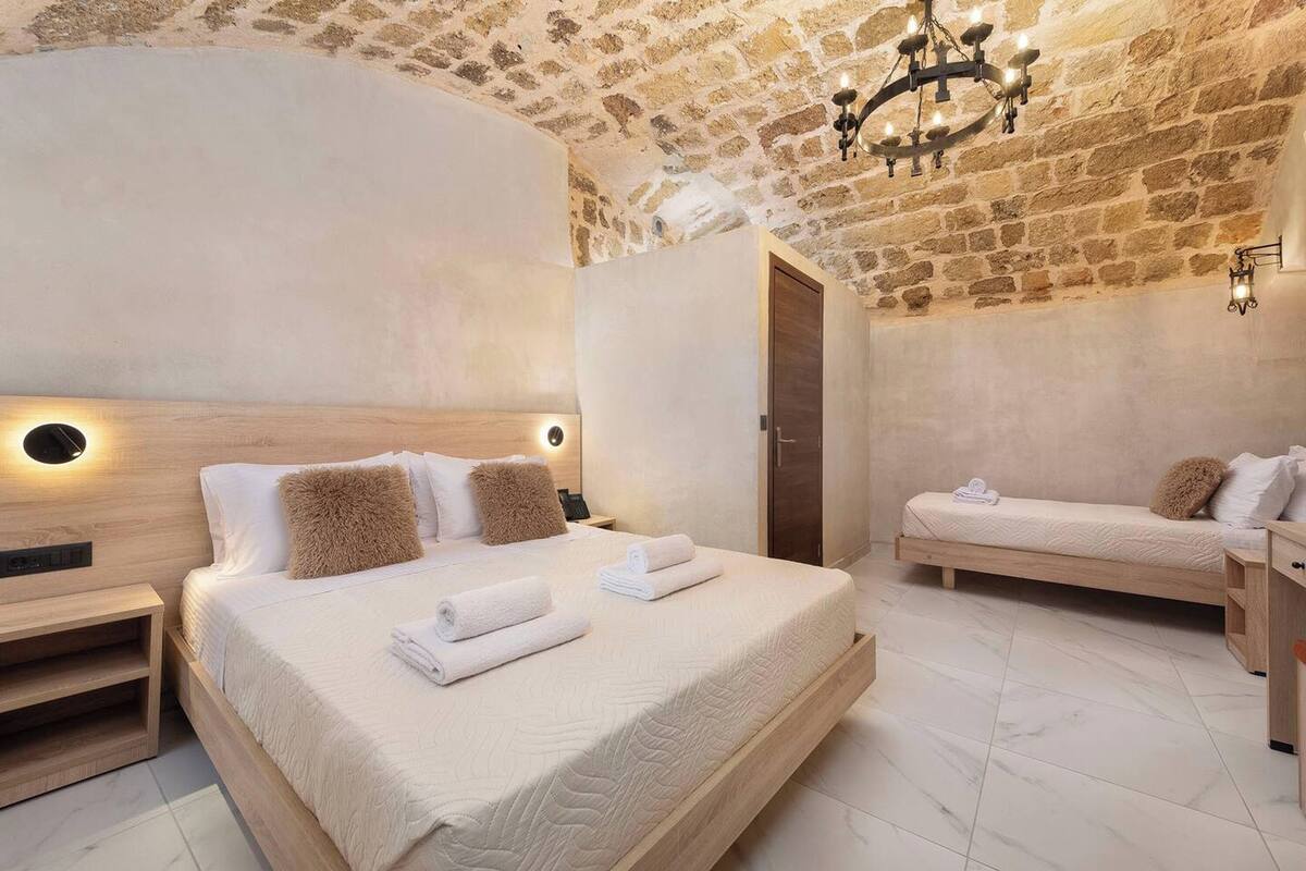 A bedroom with a stone ceiling, a large bed with white bedding, a smaller bed, and a wooden nightstand.
