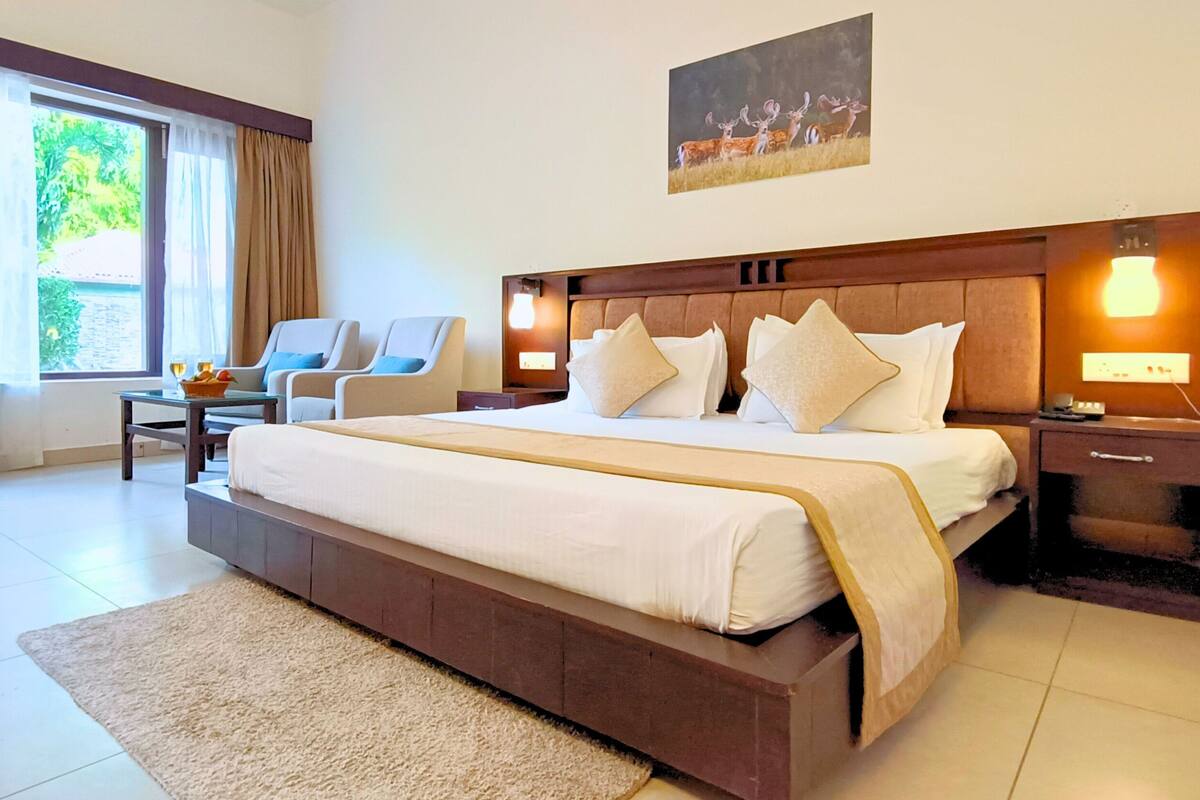 Ruime slaapkamer met een groot bed, twee nachtkastjes, een stoel en een raam met gordijnen.