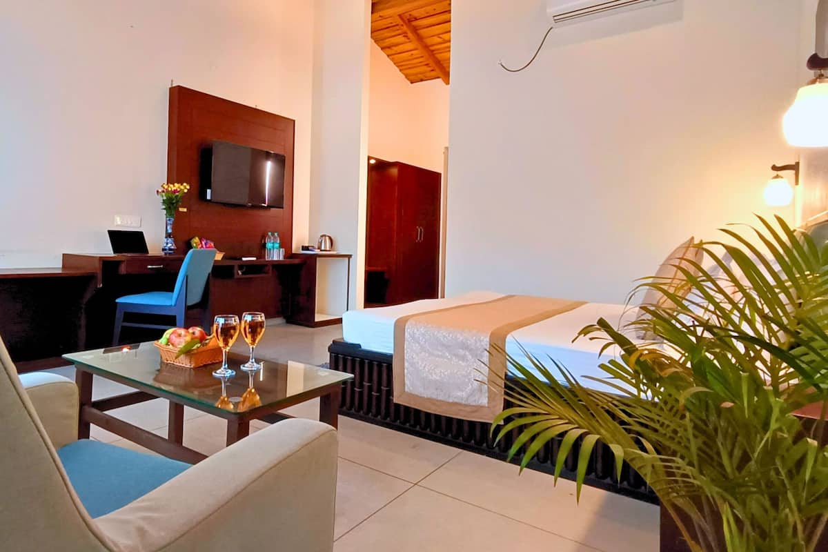 Hotelkamer met een bed, bureau met laptop, stoel, glazen tafel met fruitmand en glaasjes, televisie en een potplant.