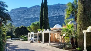 A gravel driveway leading to a building with white columns and a dome structure, surrounded by greenery and mountains in the background.