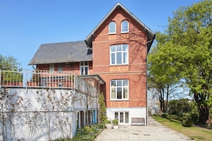 A two-story brick house with a balcony, a small garden, and a paved driveway.