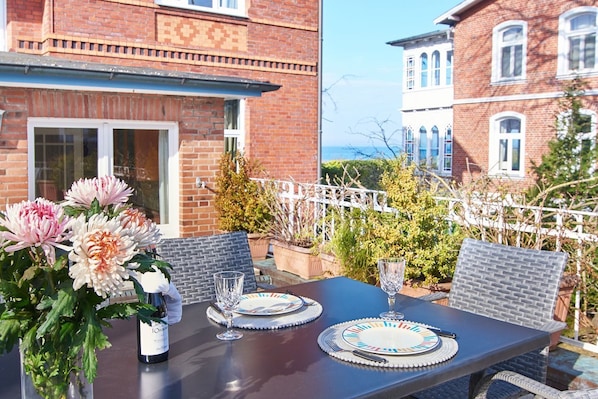 A table set outdoors with a bottle of wine, two glasses, and a vase of flowers.