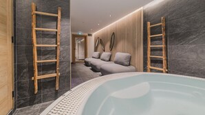 Un moderno espacio de spa con hidromasaje, escaleras de madera y una zona de estar con cojines.