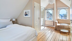 Quarto com cama, mesa de cabeceira, janela e varanda com vista.