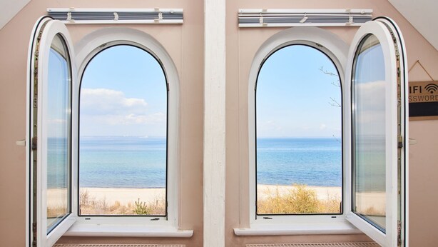 Duas janelas em arco com vista para o mar e a praia.