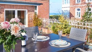 An outdoor dining area with a table set for two, surrounded by wicker chairs, a vase with flowers, and a bottle of wine. - Double room "Seestern" - Quiet time-out with sea view on the second floor - (Timmendorfer Strand)