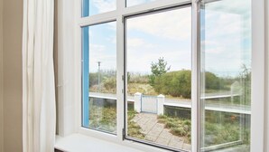 A room with a large window overlooking a paved area with a gate and vegetation. - Double room "Seestern" - Quiet time-out with sea view on the second floor - (Timmendorfer Strand)